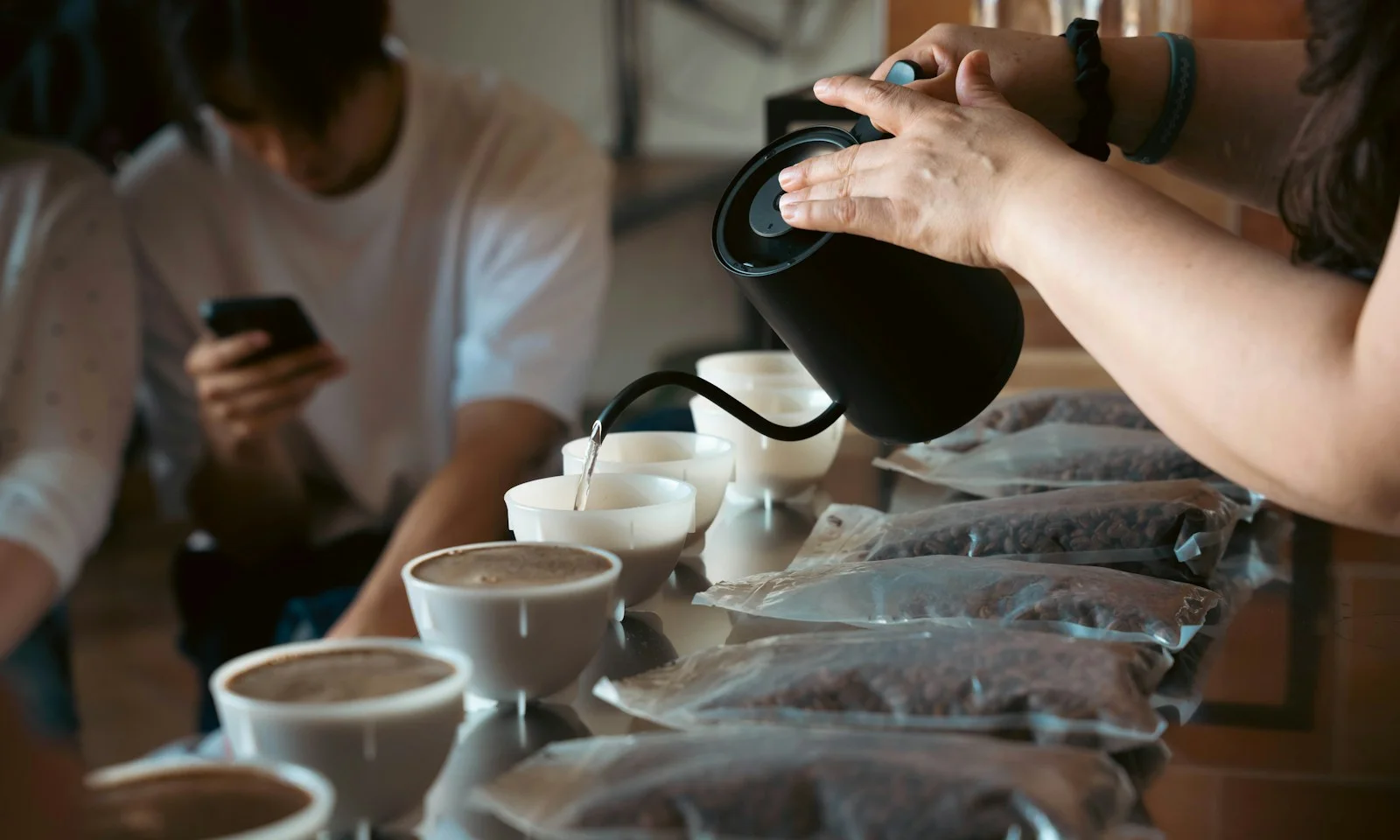 Coffee cupping water poured from a gooseneck kettle into white tasting bowls