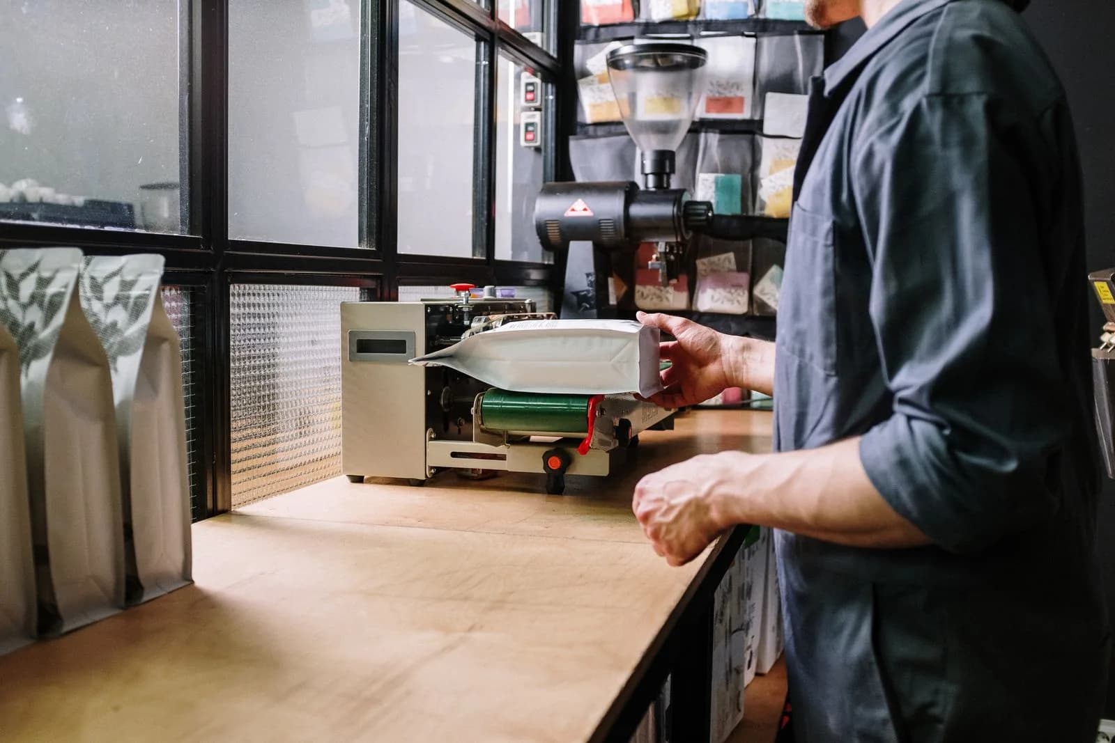 Roastery operator feeding a filled coffee bag through a band sealer