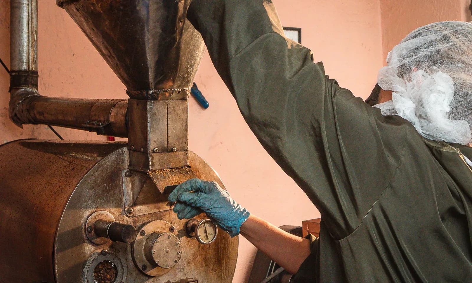 Gloved worker operating a coffee roaster, illustrating coffee roasting production planning